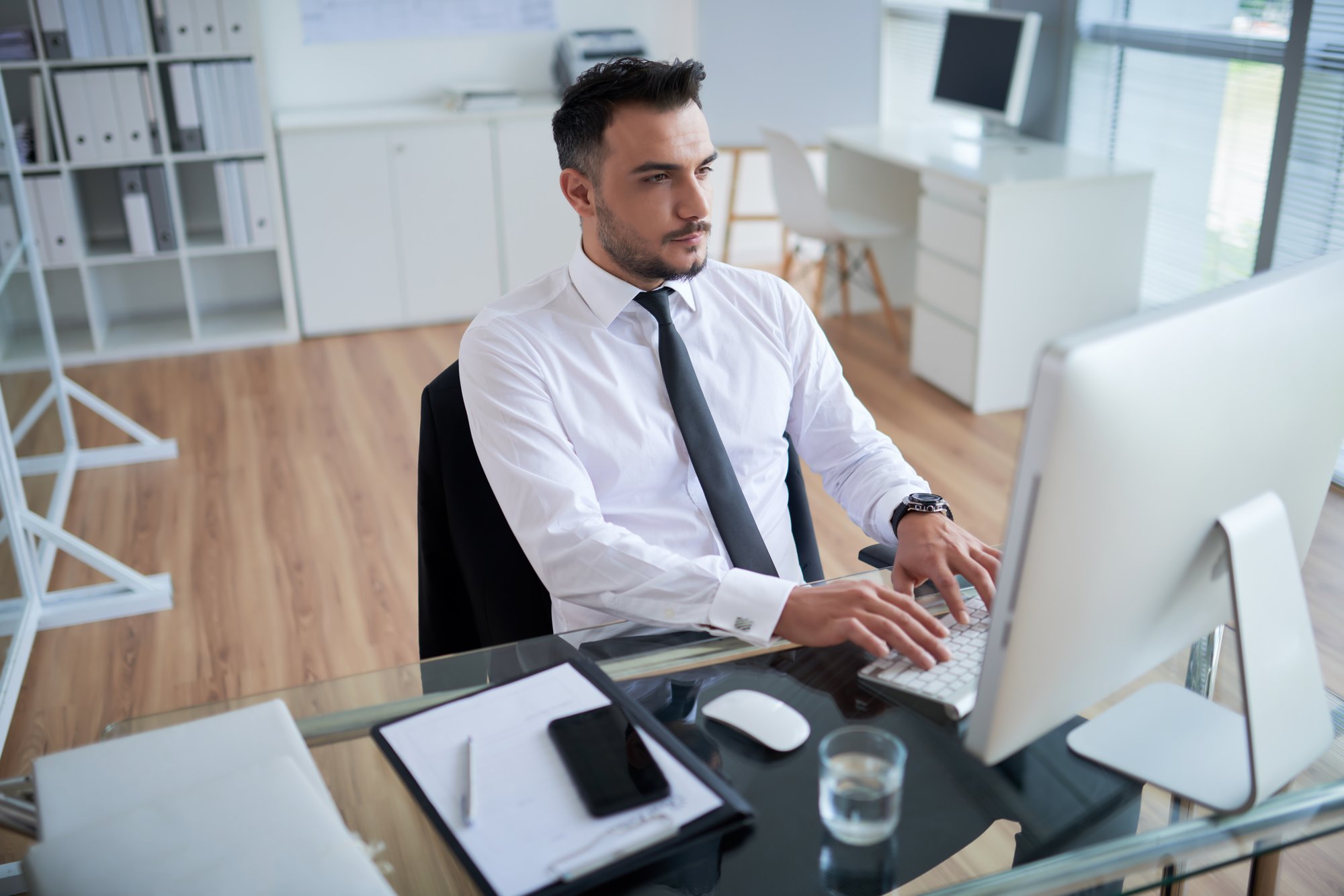 joven-caucasica-en-camisa-formal-y-corbata-sentado-en-la-oficina-y-trabajando-en-la-computadora